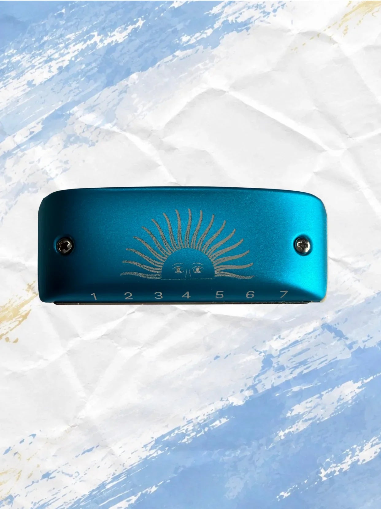 Teal harmonica with sunburst design, numbered holes, on crumpled paper background